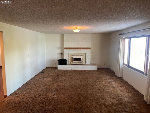 unfurnished living room featuring dark carpet, a fireplace, and a textured ceiling