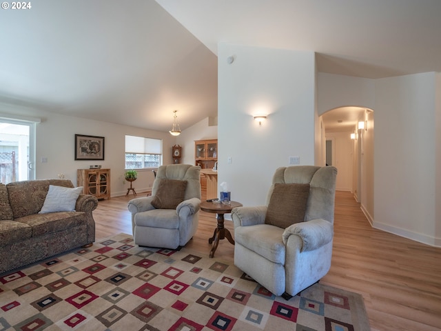 living room with arched walkways, high vaulted ceiling, light wood finished floors, and baseboards