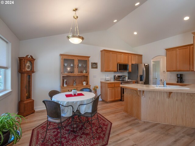 kitchen with vaulted ceiling, light wood-type flooring, stainless steel appliances, kitchen peninsula, and a breakfast bar