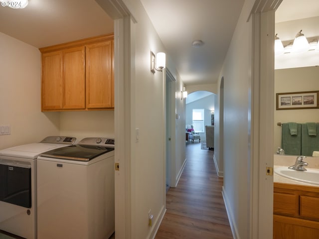 laundry room featuring arched walkways, washing machine and dryer, dark wood-style flooring, a sink, and cabinet space