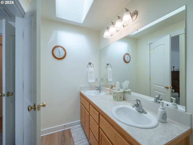 bathroom featuring double vanity, a skylight, baseboards, and a sink