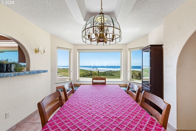 tiled dining room with a notable chandelier, a water view, a textured ceiling, and a healthy amount of sunlight