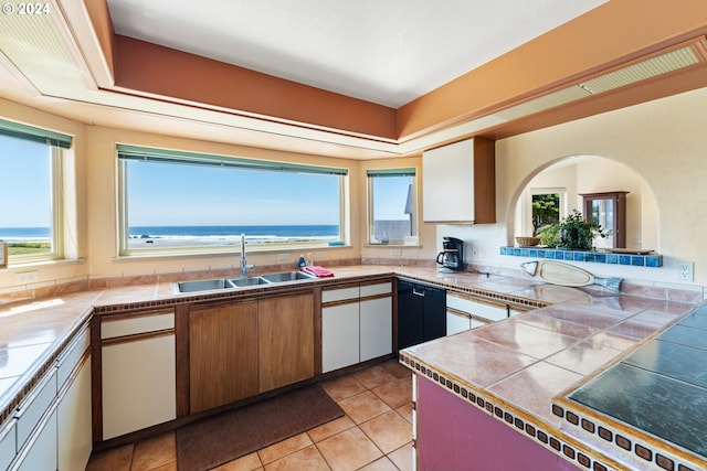 kitchen with white cabinets, sink, dishwasher, tile counters, and a water view