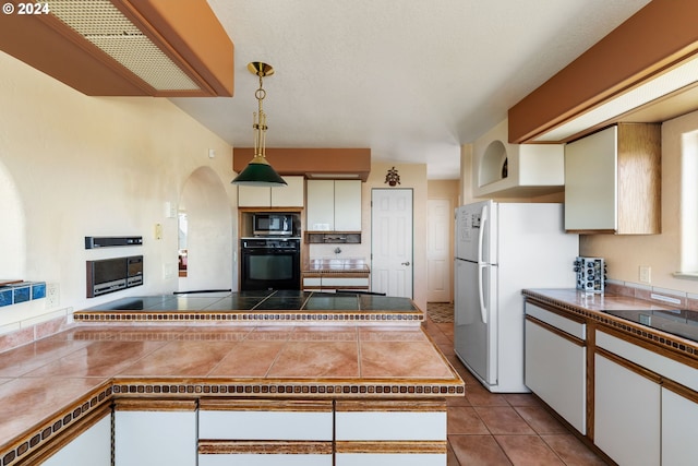 kitchen featuring white cabinetry, hanging light fixtures, a fireplace, black appliances, and tile countertops