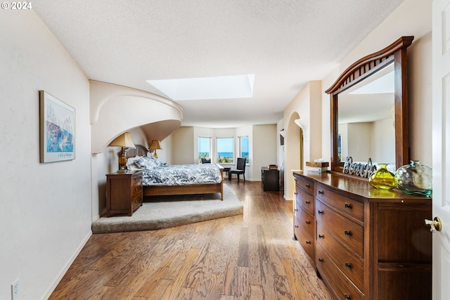 bedroom with a textured ceiling, hardwood / wood-style floors, and a skylight