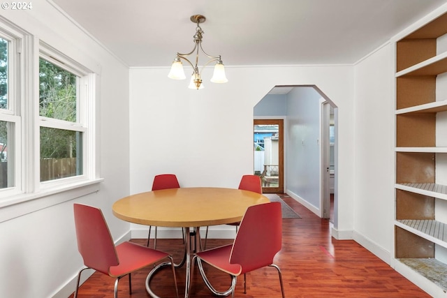 dining area with dark wood-type flooring, crown molding, and a chandelier