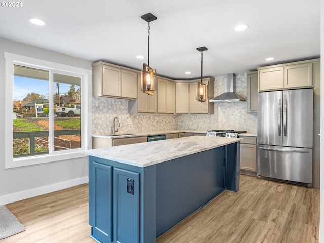 kitchen featuring appliances with stainless steel finishes, decorative light fixtures, wall chimney exhaust hood, and light hardwood / wood-style floors