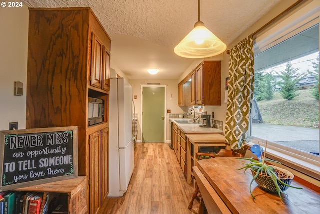 kitchen with a textured ceiling, sink, white refrigerator, light hardwood / wood-style flooring, and hanging light fixtures