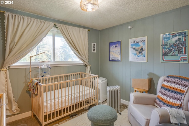 carpeted bedroom with a crib, a textured ceiling, and radiator