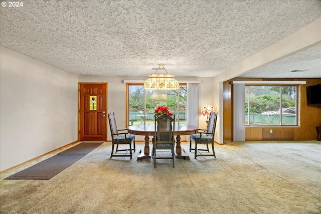 dining area with carpet flooring, a textured ceiling, an inviting chandelier, and wooden walls