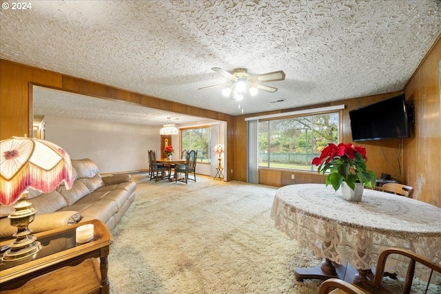 living room featuring carpet flooring, ceiling fan, wood walls, and a textured ceiling