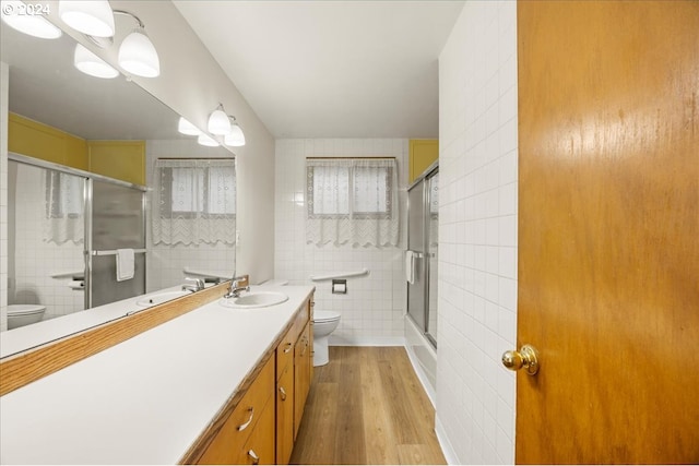 full bathroom featuring hardwood / wood-style floors, vanity, combined bath / shower with glass door, toilet, and tile walls