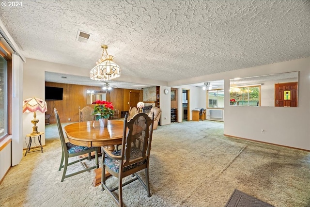 carpeted dining area with ceiling fan with notable chandelier, a textured ceiling, and wood walls