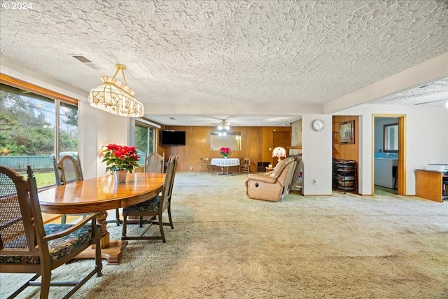 carpeted dining room featuring ceiling fan with notable chandelier, washer / dryer, a textured ceiling, and wood walls