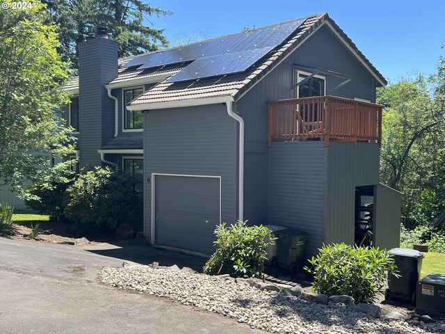 view of side of property with a garage, solar panels, and a balcony