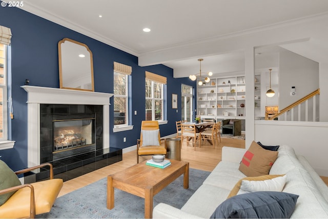 living room featuring hardwood / wood-style flooring, built in features, a fireplace, ornamental molding, and a chandelier