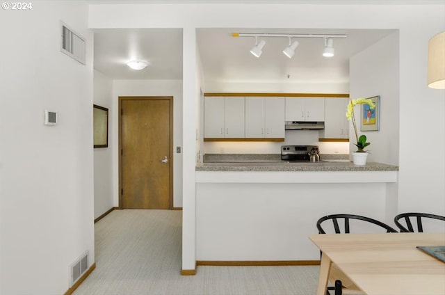 kitchen featuring track lighting, light colored carpet, decorative light fixtures, white cabinets, and stainless steel stove