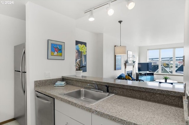 kitchen with appliances with stainless steel finishes, rail lighting, sink, white cabinetry, and hanging light fixtures