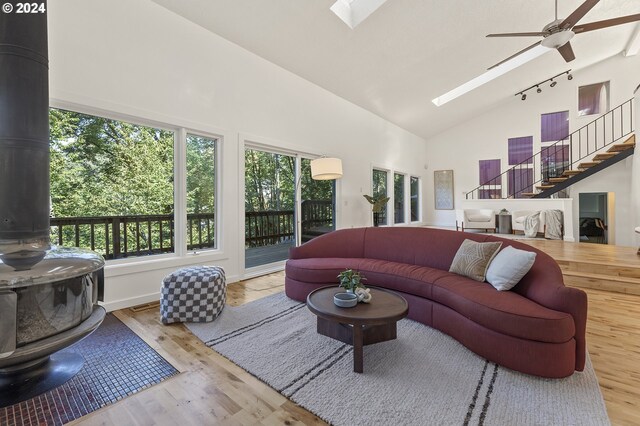 living room with light hardwood / wood-style flooring, a wood stove, a skylight, high vaulted ceiling, and ceiling fan