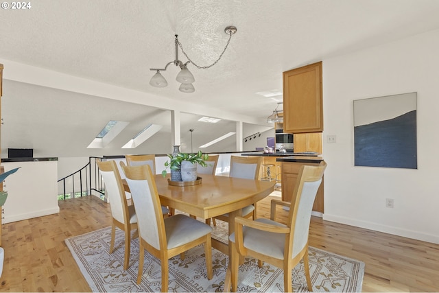 dining room featuring a skylight, a notable chandelier, a textured ceiling, and light hardwood / wood-style flooring