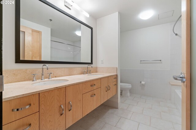 full bathroom with washtub / shower combination, dual vanity, toilet, tile walls, and tile patterned floors