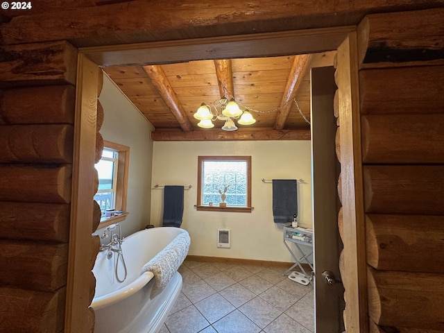 bathroom with a notable chandelier, a soaking tub, tile patterned flooring, beamed ceiling, and baseboards