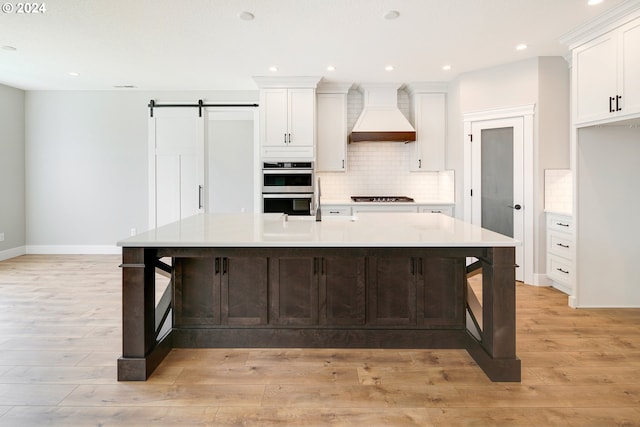 kitchen with light wood-type flooring, custom range hood, backsplash, white cabinets, and double oven