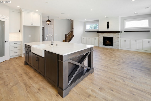 kitchen featuring light hardwood / wood-style floors, white cabinetry, an island with sink, a stone fireplace, and sink