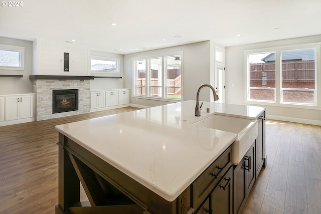 kitchen featuring a stone fireplace, a kitchen island with sink, a wealth of natural light, and hardwood / wood-style floors