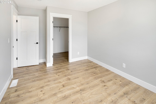 unfurnished bedroom with a walk in closet, a closet, and light wood-type flooring