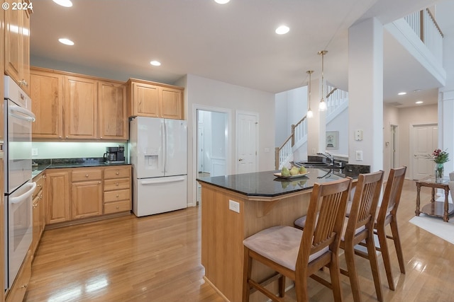 kitchen featuring kitchen peninsula, pendant lighting, light hardwood / wood-style floors, white appliances, and a kitchen bar