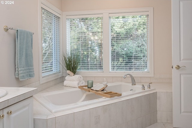 bathroom featuring plenty of natural light, tiled tub, and vanity