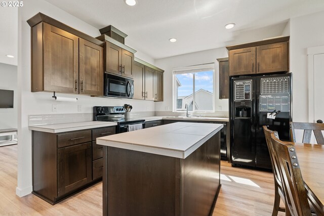 kitchen featuring black appliances, light countertops, light wood-style flooring, a kitchen island, and dark brown cabinets