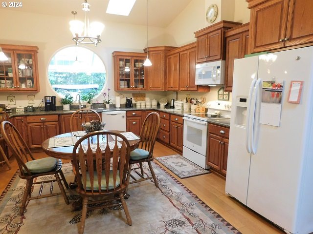 kitchen featuring pendant lighting, light wood-type flooring, a chandelier, vaulted ceiling with skylight, and white appliances