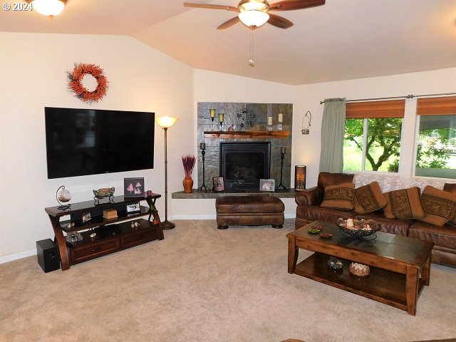 carpeted living room featuring lofted ceiling, a tiled fireplace, and ceiling fan