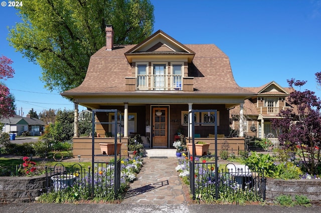 view of front of house with a chimney, a porch, a shingled roof, fence, and a balcony