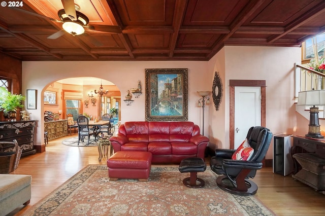 living room with ceiling fan with notable chandelier, arched walkways, coffered ceiling, and wood finished floors