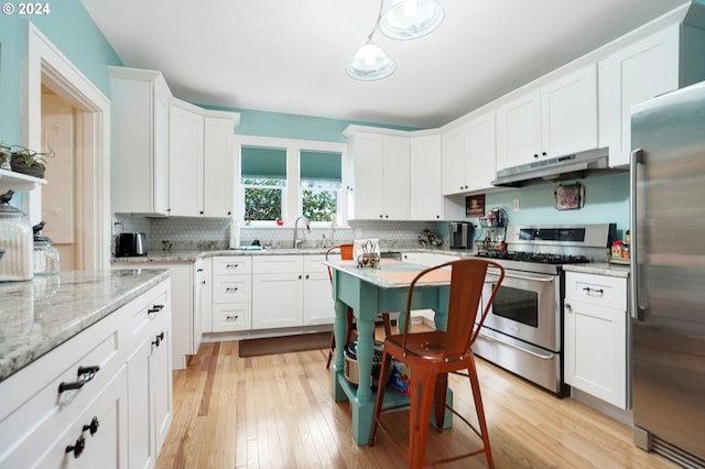 kitchen with white cabinets, under cabinet range hood, stainless steel appliances, and decorative backsplash