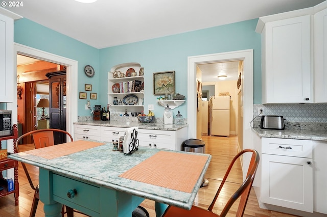 kitchen with stainless steel microwave, light wood-type flooring, freestanding refrigerator, and white cabinetry