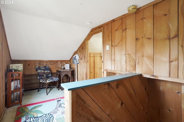 interior space featuring light carpet, vaulted ceiling, and wooden walls