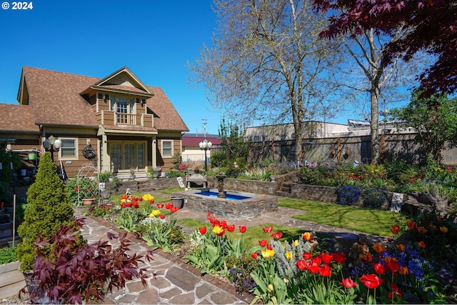 back of property featuring a hot tub, a fenced backyard, a shingled roof, and a balcony