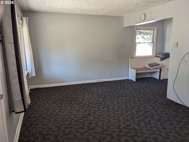 unfurnished room with dark colored carpet and a textured ceiling