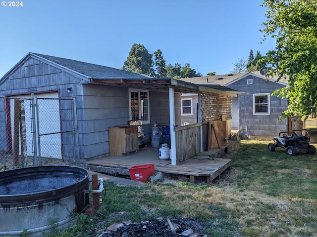 rear view of property with an outbuilding, a wooden deck, a lawn, and a jacuzzi