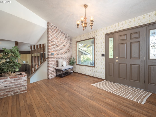 foyer with a chandelier, vaulted ceiling, stairway, hardwood / wood-style floors, and wallpapered walls