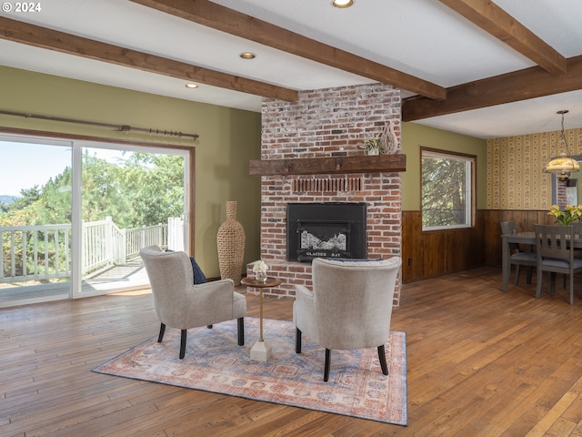 living area with a brick fireplace, wainscoting, beamed ceiling, and hardwood / wood-style floors