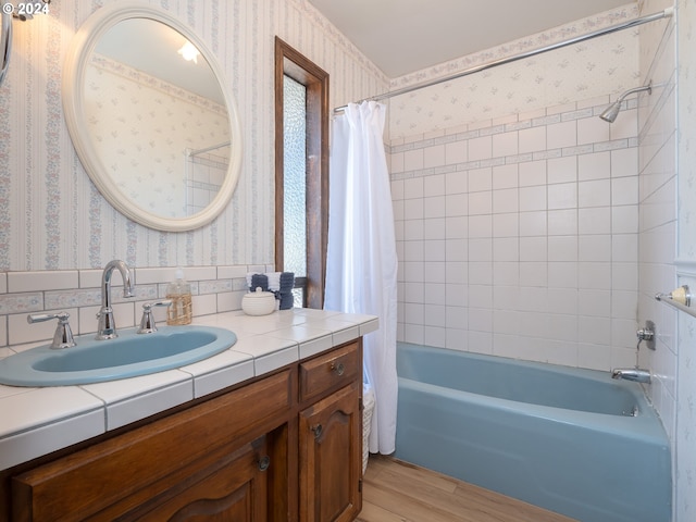 bathroom featuring shower / bathtub combination with curtain, wood finished floors, vanity, and wallpapered walls