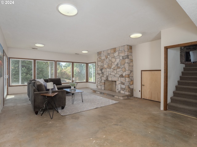 living area featuring concrete flooring, stairway, and a stone fireplace