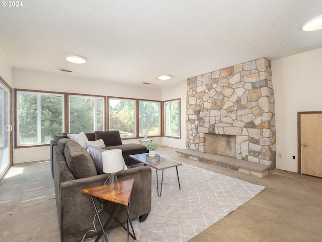 living area featuring concrete flooring, a healthy amount of sunlight, a stone fireplace, and a textured ceiling