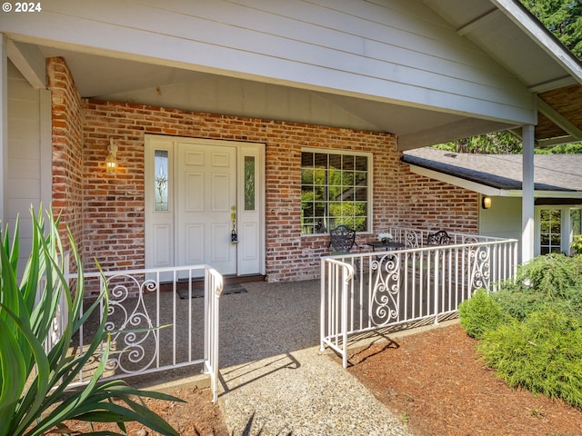 view of exterior entry featuring a porch and brick siding