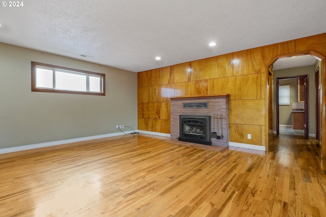 unfurnished living room with a fireplace, a textured ceiling, light hardwood / wood-style floors, and wooden walls